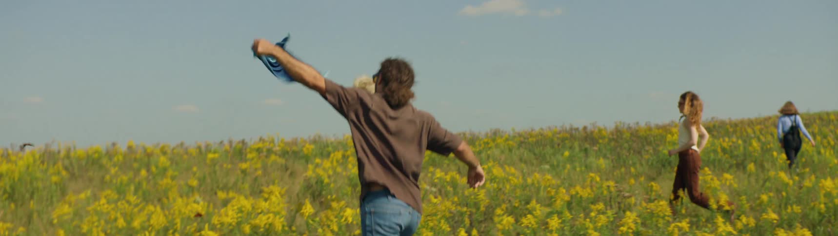 Four teenager walk and run through a field of flowers while one waves a piece of fabric in the air