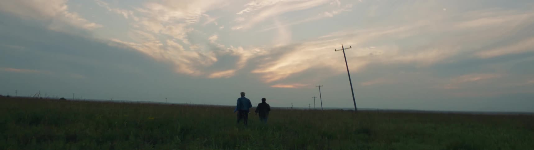 Friends running across a pasture in the country towards the sunset