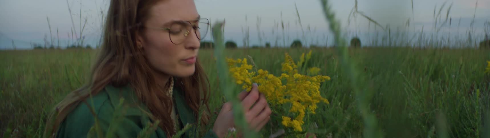 A woman is walking through a field and looking at flowers