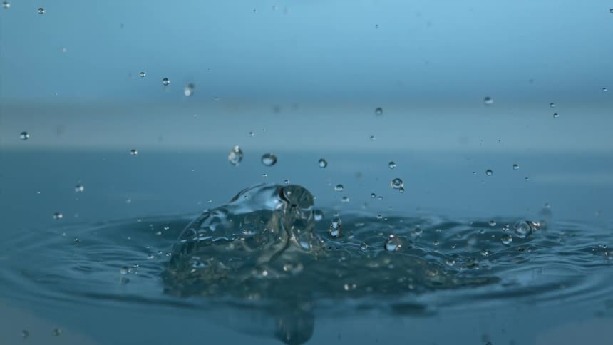 Clear spheres fall down in a blue environment and splash with liquid flying and droplets floating in the air as they fall