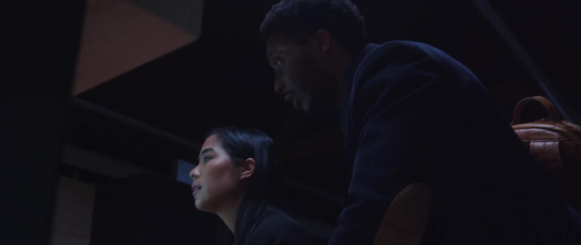 A woman sitting in front of a computer in an office turns and talks to a man behind her who is also looking at the screen