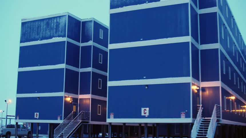 A man on a construction site stands by a truck and then walks towards a building