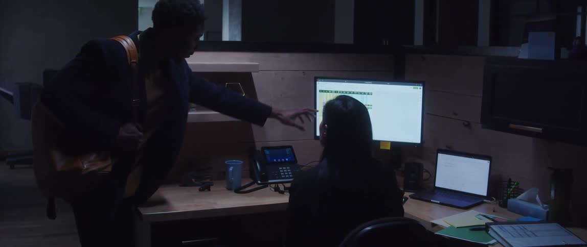 A man pointing to a computer screen that a women is in front of sitting at her desk