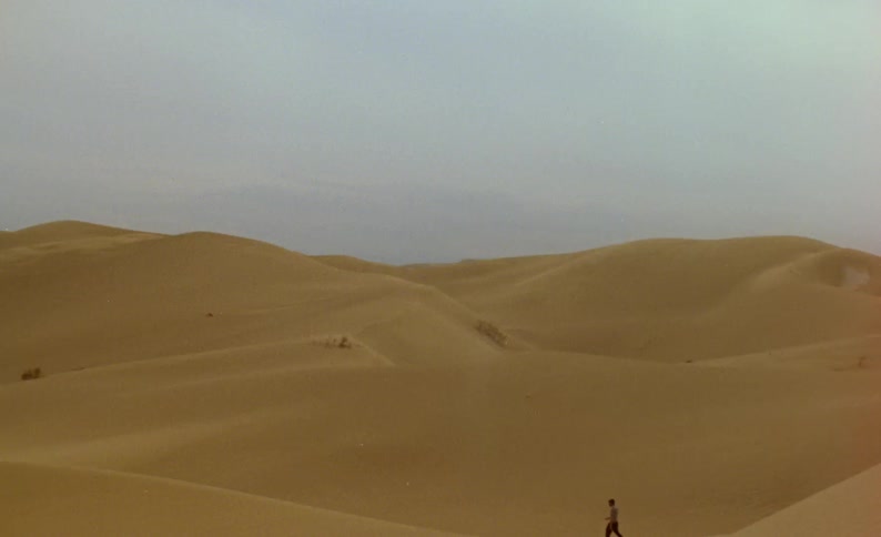 A man walks across a sand dune in the desert