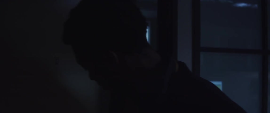 A man with a bag over his shoulder opens a door and walks inside a room with a computer on the desk