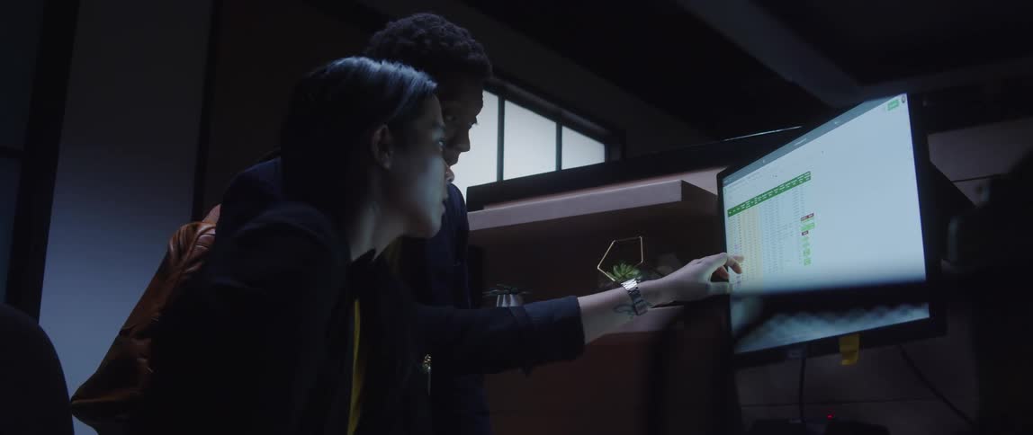 Two people discuss a spreadsheet in an office cubicle