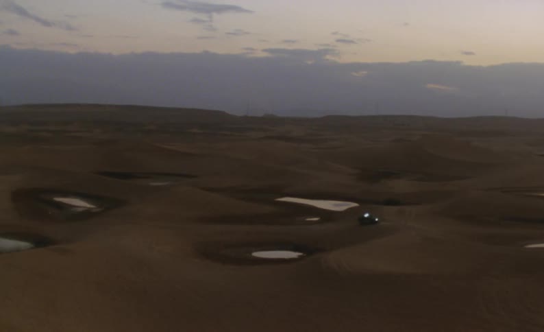 A vehicle drives across sandy dunes