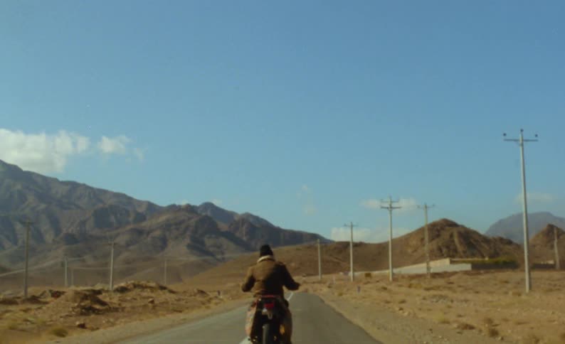 A man rides a motorbike toward a mountain range