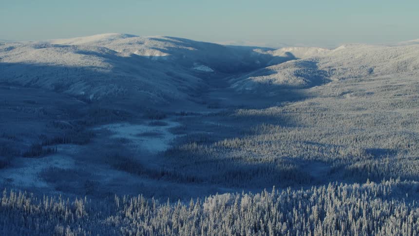 An aerial view of forest covered hills mountains and valleys with shadows cast through the valley