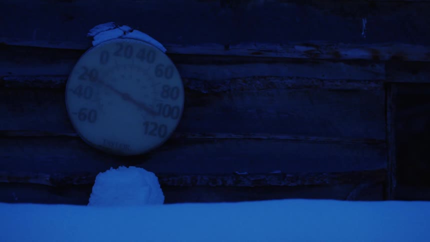 A circular thermometer on the side of a building covered and surrounded by snow