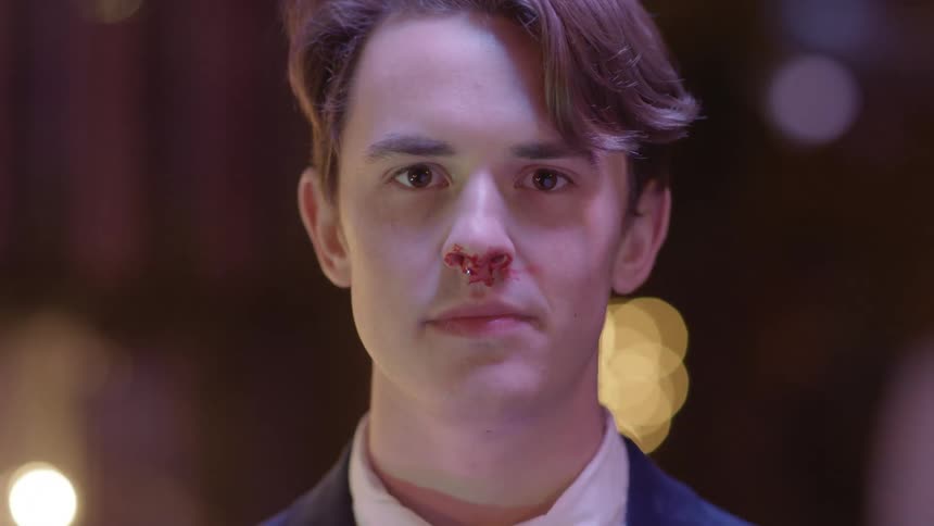 Light shines on the face of a young man standing in a room with lights in the distance