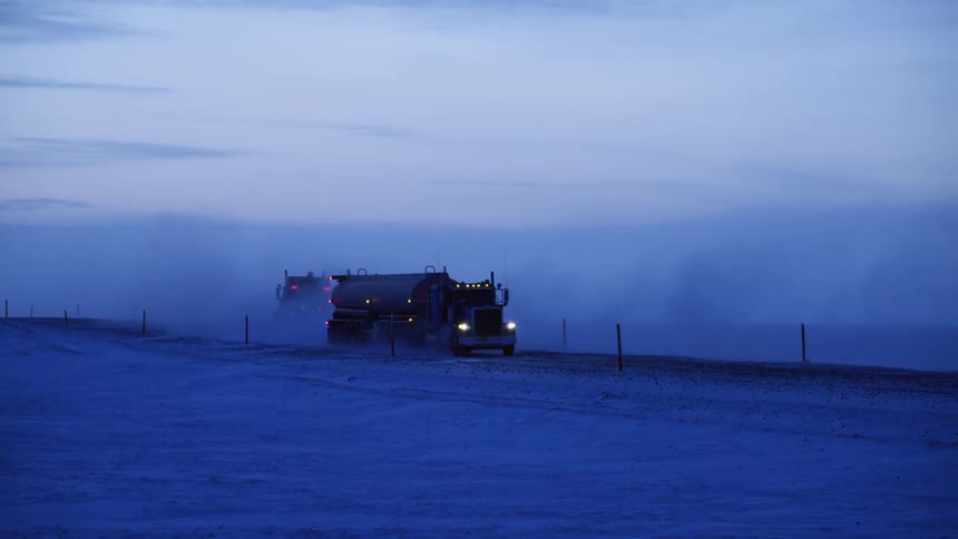 A tanker truck passes another truck on a snow covered rural road
