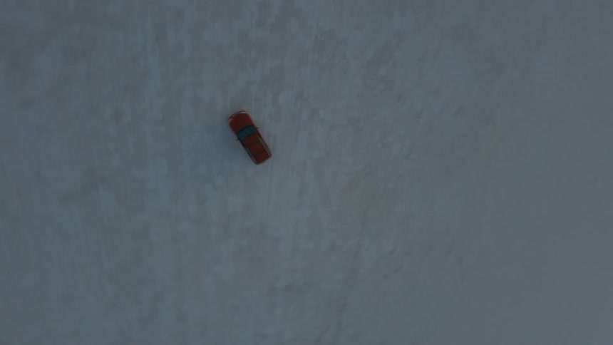 Aerial drone shot following a red car driving on the flat white sands of a desert at sunset