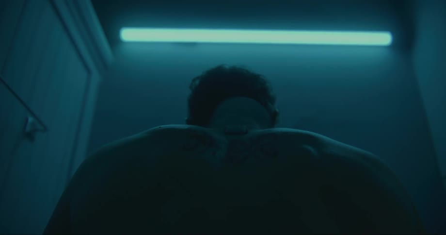 Rising back of a shirtless man reclined on the bathroom sink under a blue light
