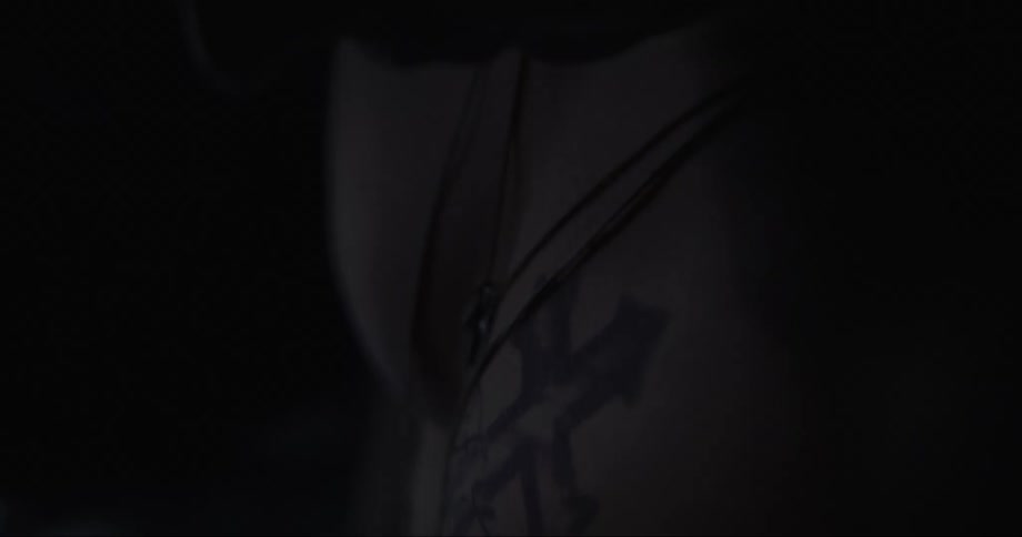 Man with tattoo hangs his head in dark room