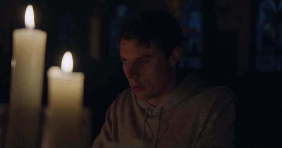 A man is sitting in a dark room illuminated with candles