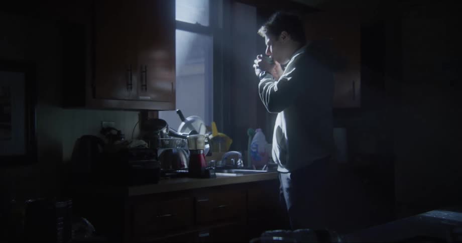Man walks to the kitchen countertop and grabs a cup of hot coffee looks out the kitchen window and takes a sip of coffee then turns around and looks in the room