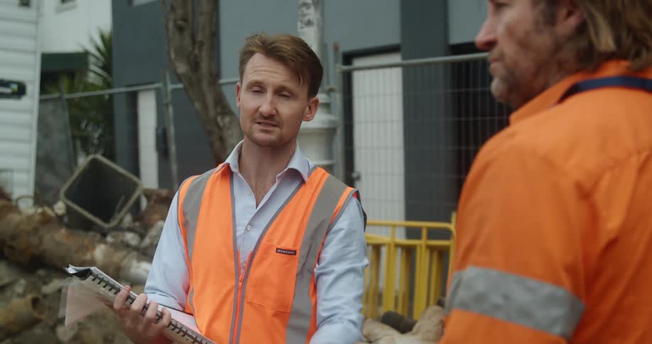 Road workers consult notebook near building