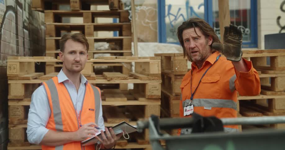 Two men stand outside and discuss construction plans