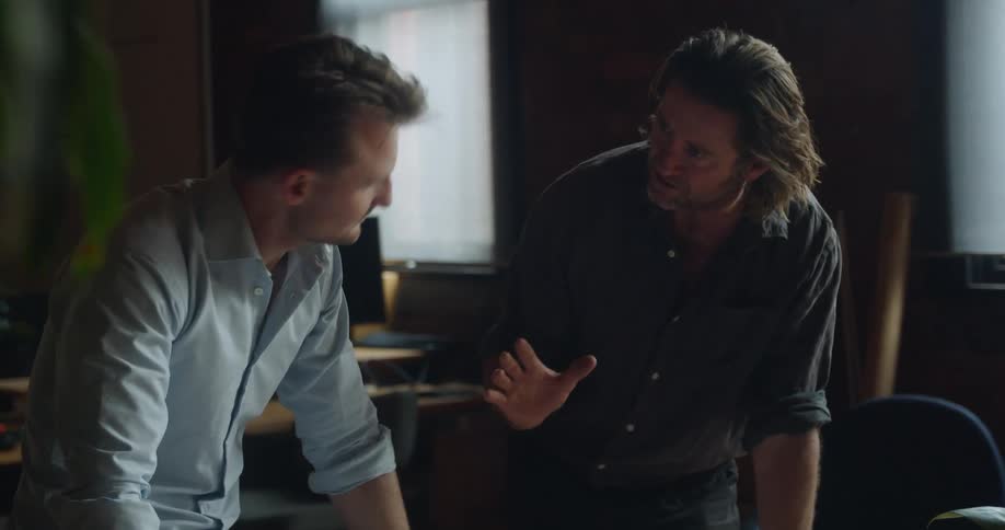 A pair of men discuss a blueprint lying on a desk in front of them in an office during the day