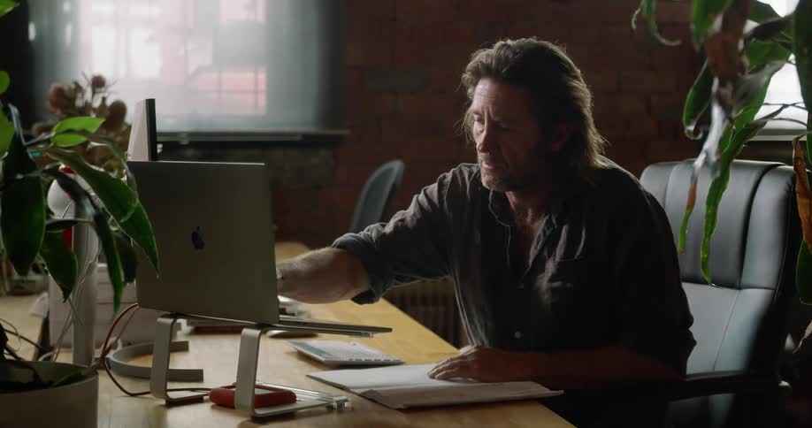A man writes on blueprints after pressing a touch screen monitor all while thinking deeply