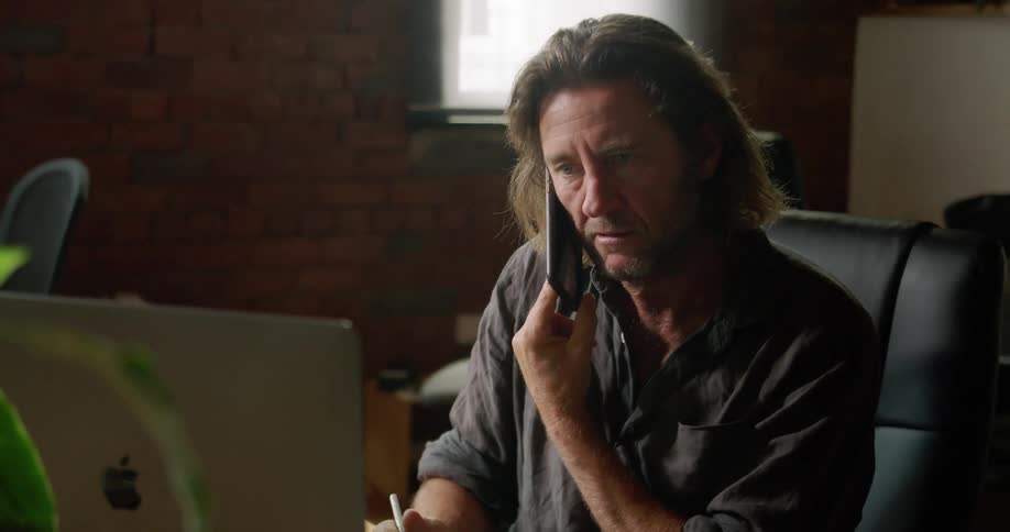 A man talks to someone while reading something off his laptop