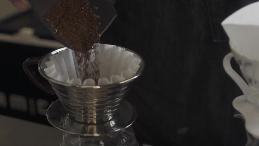 Someone pours coffee grounds into a filter