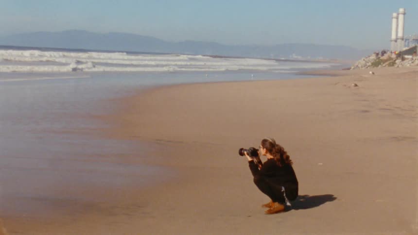 A woman crouches along the shore and takes photos of the ocean