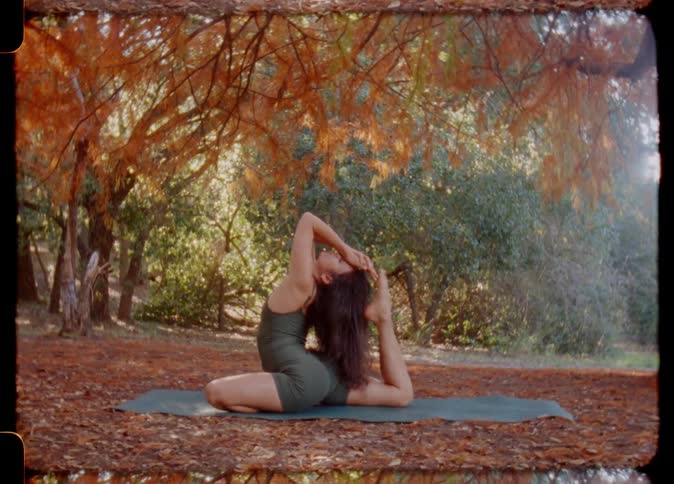 A woman stretches her neck and head while doing yoga in a park