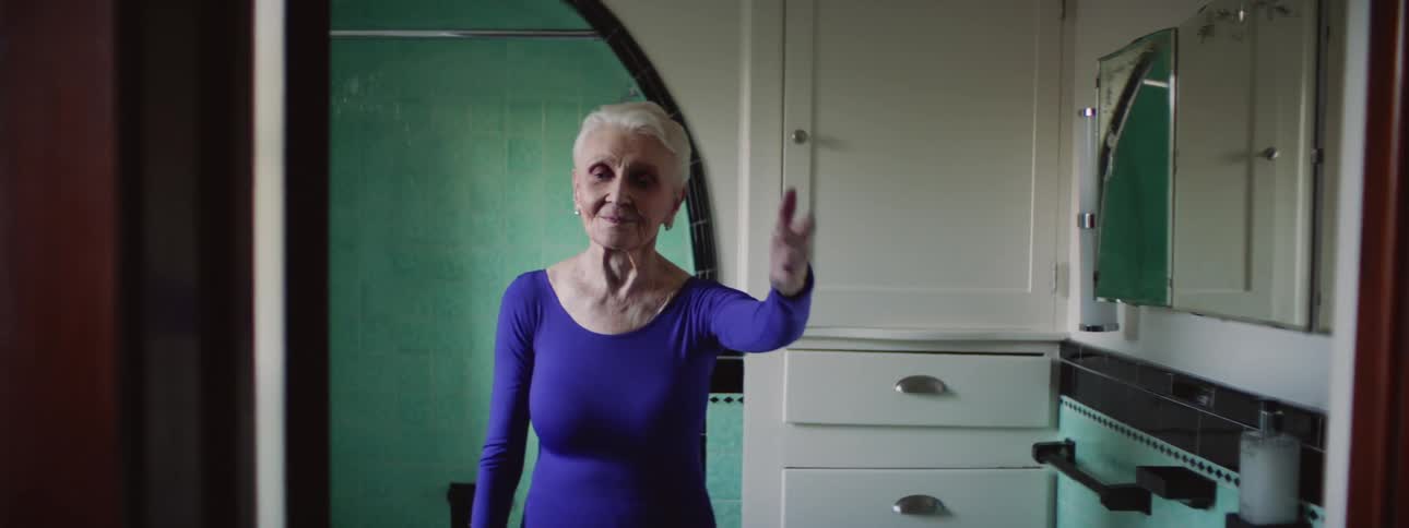 Elderly woman wearing leotard dances in home