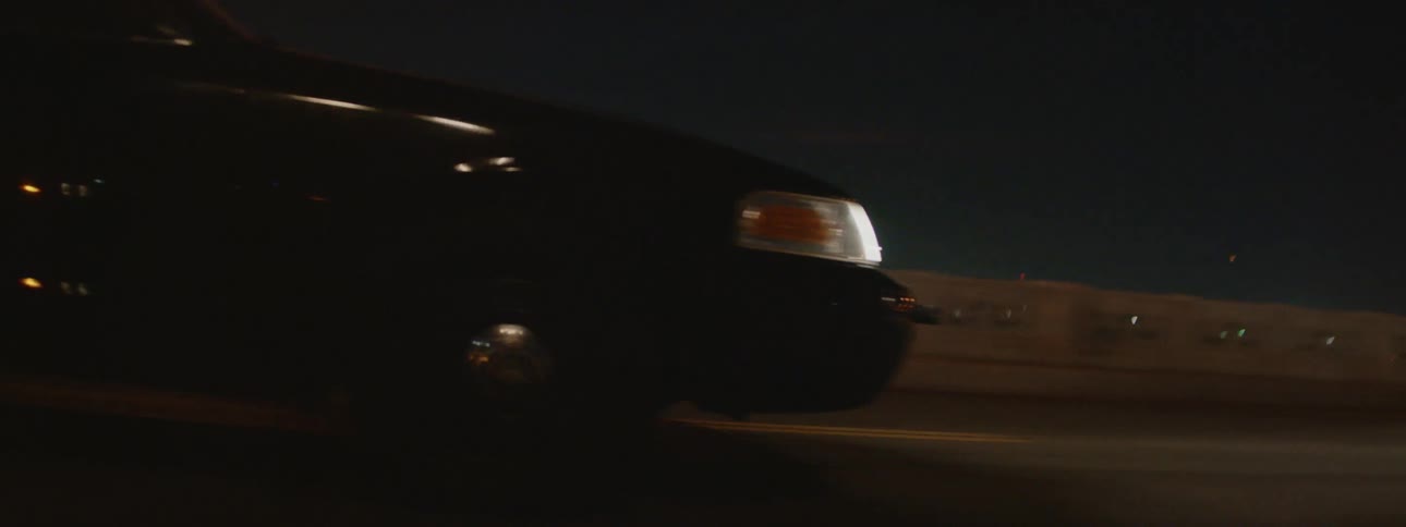 Street lights illuminate the road as a black automobile travels into town as city lights shine