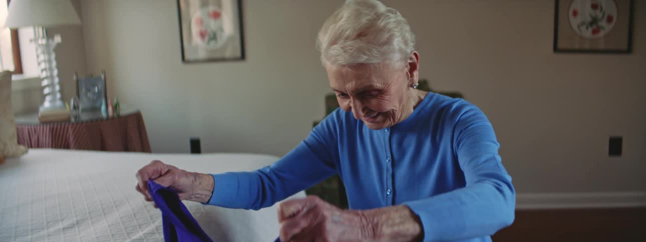 An elderly woman taking a piece of clothing from a memory box and smiling while she holds it up to her body