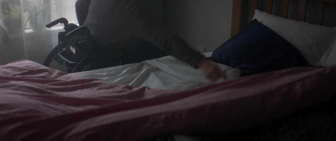 Blonde woman in wheelchair makes bed in bedroom