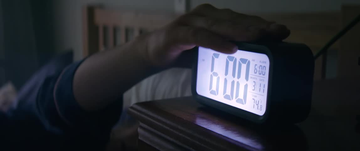 Woman wakes up and turns off digital alarm clock in bedroom