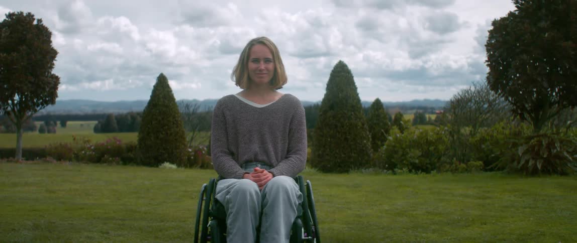 A women in a wheelchair sitting in a grassy lawn on a cloudy day