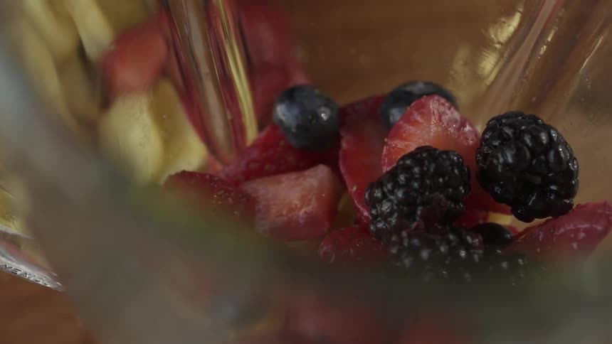 Someone drops fruit into a blender