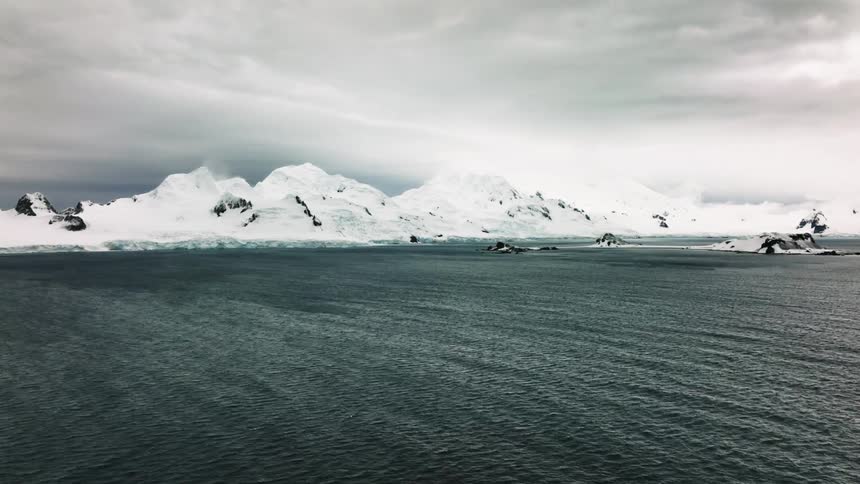 Waves roll toward snow covered shore under and overcast sky hyperlapse