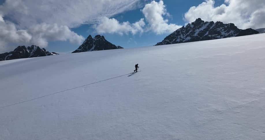 A person wearing a backpack is walking up a snow covered mountain with skis and trekking poles