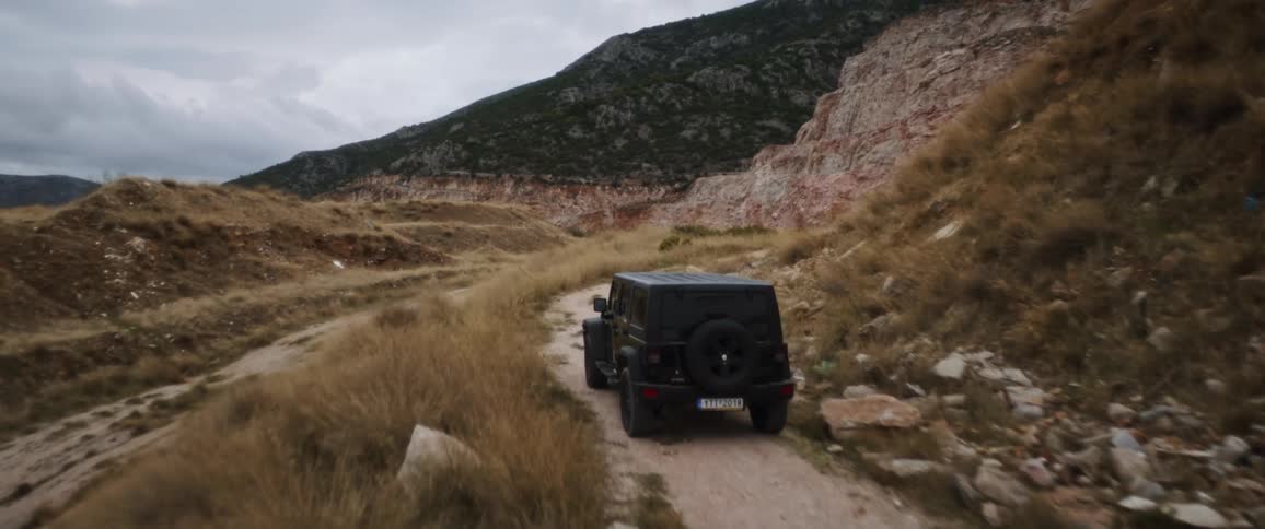 A jeep drives on a rocky road by a mountain range