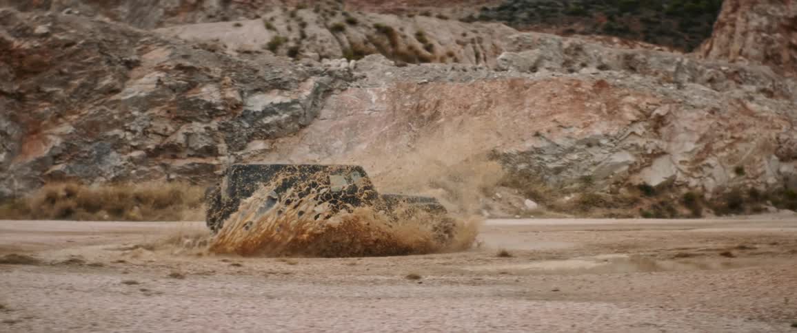 A black jeep is traveling on a desert mountain dirt road and it splashes water as it goes through a puddle