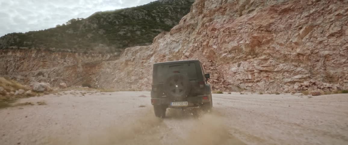 A black jeep driving through a sandy dirt road between rocky mountain canyons