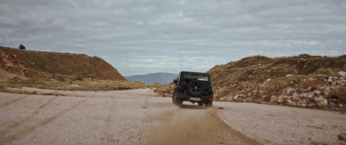 A black jeep drifting and spinning up dirt on a desert road between rocky mountains