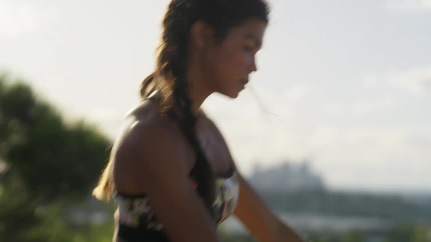 A woman sways back and forth as she stretches and exercises on a grass ridge