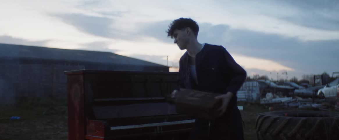 Male aggressively pouring gasoline on a piano outdoors at sunset