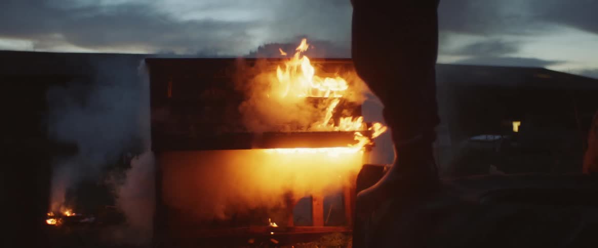 Someone is standing outside on truck tires as they watch a piano burning