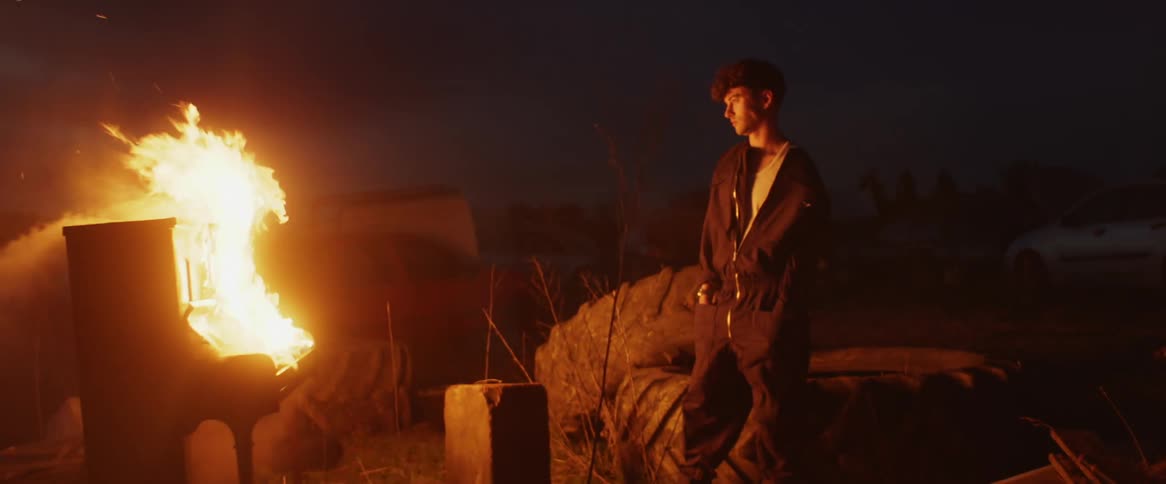 Man watches burning upright piano at night