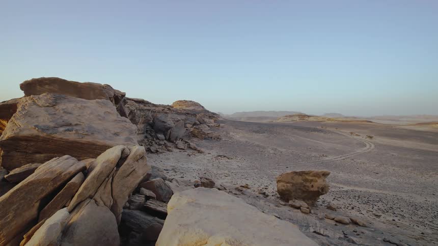 A right pan of a desert horizon with boulders and a dirt road in Saudi Arabia
