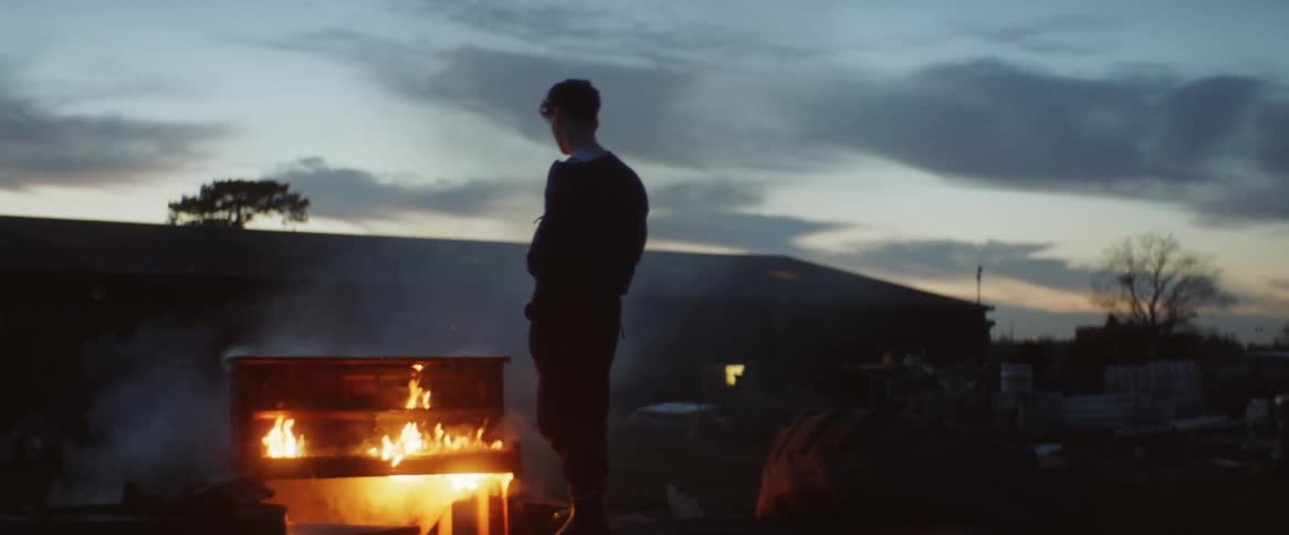 A males silhouette standing in front of a fire at dusk