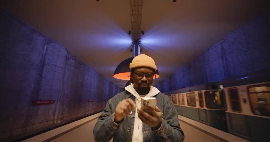 A man standing in a train station taps his cell phone as a train drives past
