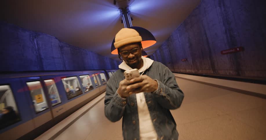 A man smiling while standing on a train platform texting